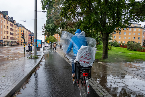 Stockholm, Sweden Sept 1, 2023 A man bicycles with a plastic rain poncho in the Hornstull district in a rain storm