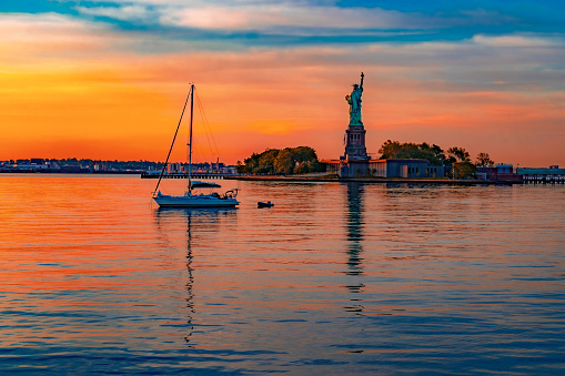 Sail boat anchored behind the Statue of Liberty on a colorful summer morning.