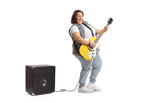 Corpulent young female with an electric guitar and amplifier isolated on white background