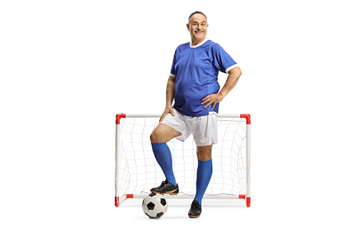 Full length portrait of a mature man in a football jersey posing in front of a minin goal isolated on white background