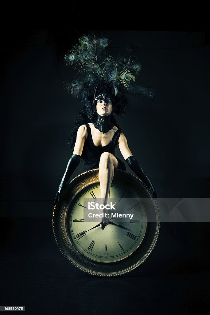 Time Performance Art Portrait Woman with extraordinary Peacock Feather Hat performing with a huge wall clock, showing the time with her leg. Surreal. Bizarre Performance Art Portrait. Dancing Stock Photo