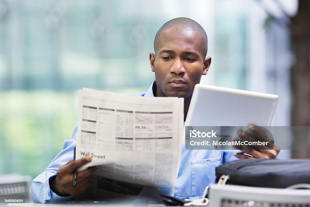 Investor compares quotes from newspaper and tablet African American businessman comparing stock market quotes on his tablet and in the newspaper. Newspaper Stock Photo