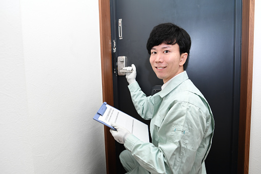 A male Asian worker repairs, replaces, and investigates the entrance door (key)