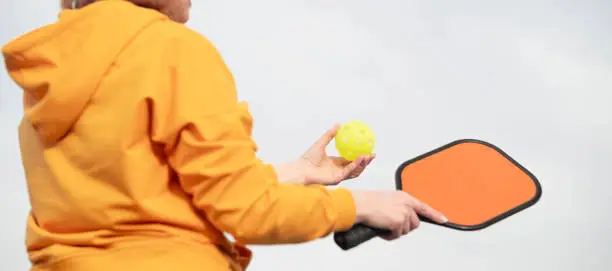 Photo of back view pickleball game woman player, hands over blue sky hitting pickleball yellow ball with paddle, outdoor sport leisure activity.