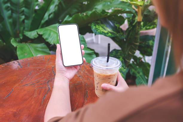 istock Mockup image of a woman holding mobile phone with blank white desktop screen while drinking coffee 1685814055