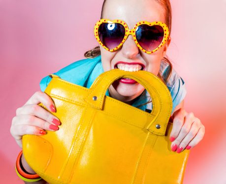 Amusing girl in funny sunglasses holding a yellow handbag in her mouth