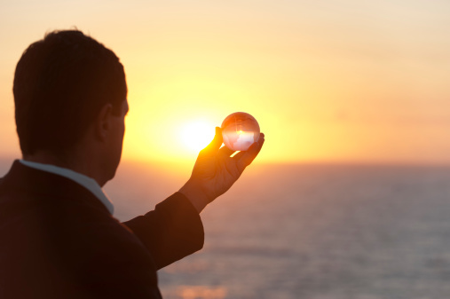 Businessman holding a world globe at dawn in silhouette over ocean