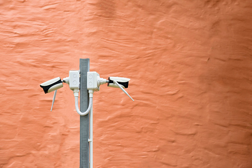 closed-circuit camera on the steel pole with brown concrete wall background .