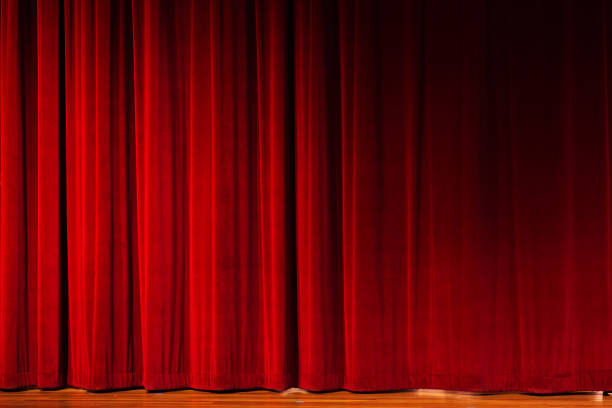 Closed red curtains over theater stage Closed red velvet stage drapes, lit by footlights, await the performer, speaker, or event. The floor of the stage is just visible. Also useful as graduated red, textured background. stage curtain up stock pictures, royalty-free photos & images
