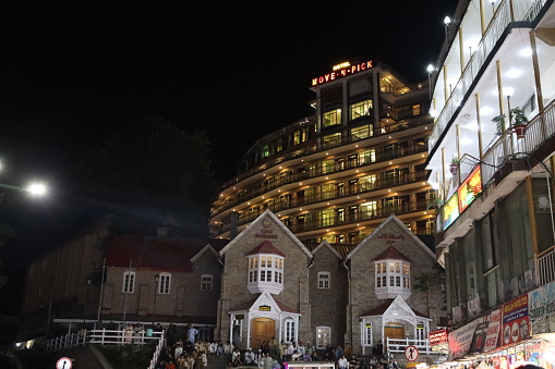In this enchanting nighttime photo, the historic GPO building in Murree radiates timeless elegance with its illuminated façade, while a medium-sized group of tourists gathered to enjoy the weather and vibrancy, creating a captivating blend of history and modernity in this charming hill station.