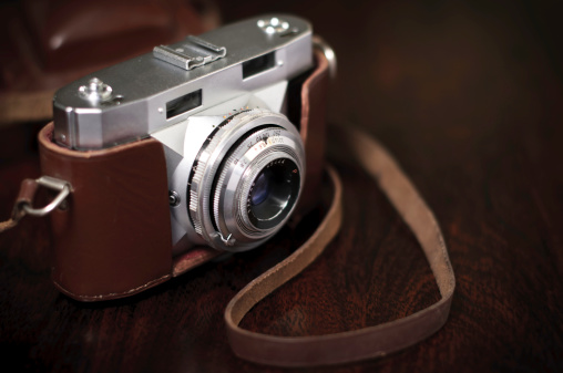 An old rare film photo camera with a lens on a brown wooden background