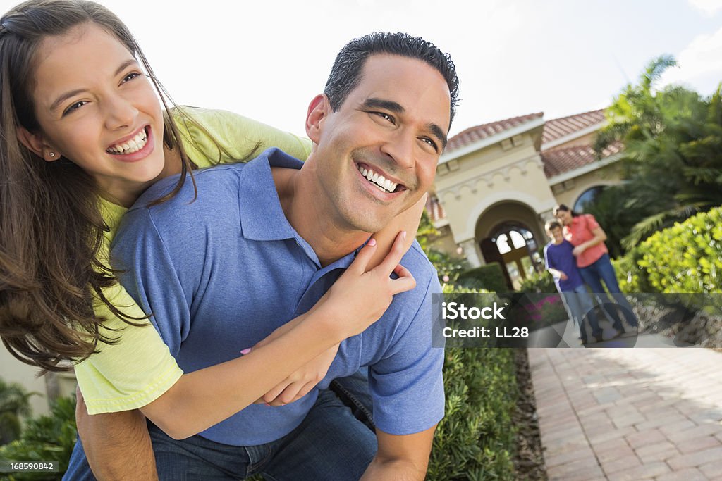 Father And Daughter Having Fun Outdoors Cheerful man carrying daughter on back with woman and son in background. Horizontal shot. 14-15 Years Stock Photo