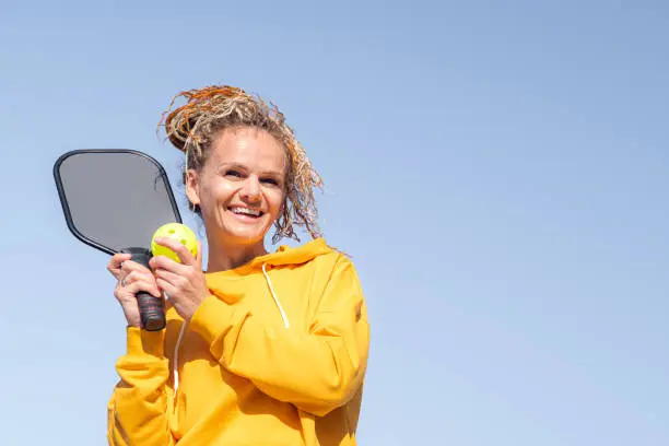 Photo of portrait woman player pickleball game over blue sky, pickleball yellow ball with paddle, outdoor sport leisure activity.