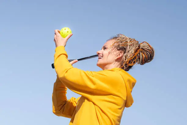 Photo of woman playing pickleball game, hitting pickleball yellow ball with paddle, outdoor sport leisure activity.