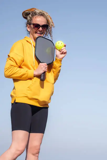 Photo of portrait woman player pickleball game over blue sky, pickleball yellow ball with paddle, outdoor sport leisure activity.