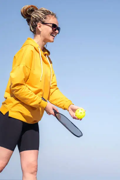 Photo of woman playing pickleball game, hitting pickleball yellow ball with paddle, outdoor sport leisure activity.