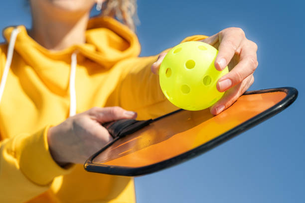 Pickleball paddle and yellow ball close up, woman playing pickleball game, hitting pickleball yellow ball with paddle, outdoor sport leisure activity. stock photo