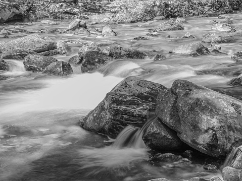 A black and white long exposure shot of a river meandering through a rocky landscape.