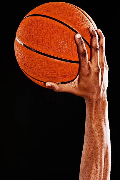 Muscular arm of a basketball player ready to shoot The muscular arm and hand of an athlete holding a basketball aloft, ready to shoot. Black background with copy space.  basketball player photos stock pictures, royalty-free photos & images