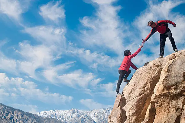 A partner puts out a helping hand up the summit.