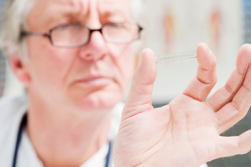 A mature medicine, holding a medical stent in his fingers. XXL size image.