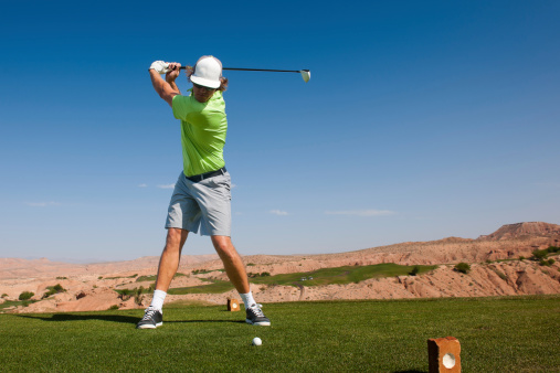 A golfer at the top of his swing teeing off in the desert.