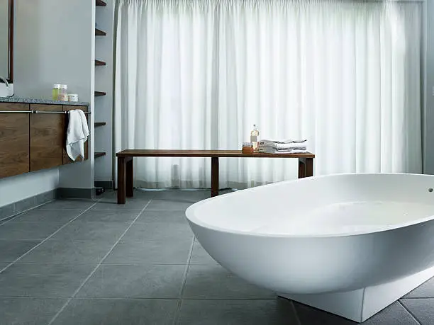 Bathtub on tiled floor with curtains and bench