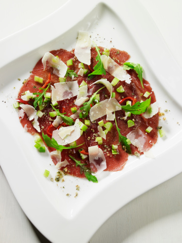 Dish with slices of bresaola, parmesan cheese and salt, pepper, spring onion, rucola salad (Eruca sativa) and olive oil. A typical Italian starter