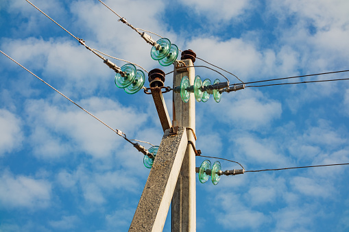 High-voltage Overhead power line with wires and insulators on a concrete pole close-up on a sunny day against a background of blue sky with clouds