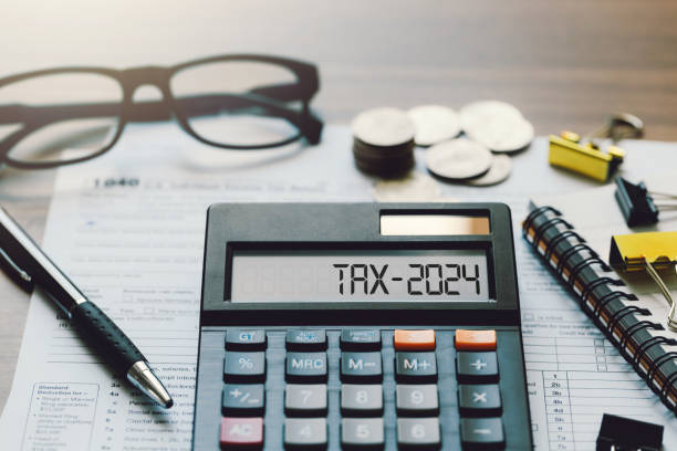 word tax 2024 on the calculator. business and tax concept.calculator, coins, book, tax form, and pen on table.tax deduction planning.financial research, government taxes, and calculation tax return - tax imagens e fotografias de stock