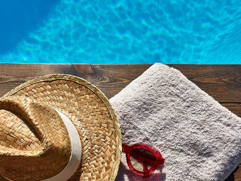 summer vacation concept. towel, hat and sunglasses on a blue hammock next to a pool on a sunny day.