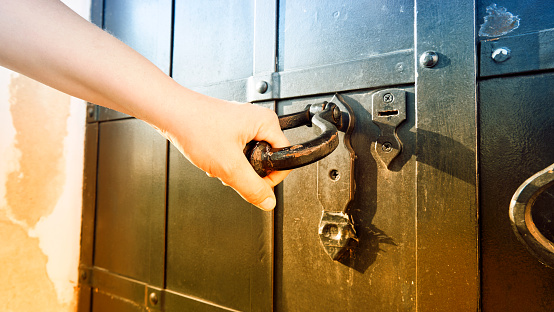 A young woman's hand opens an antique metal door. Toned image