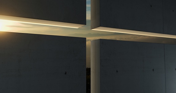 The sun casts its rays through the cross-shaped aperture in the wall of a contemporary church, filling the space with a warm and serene light.