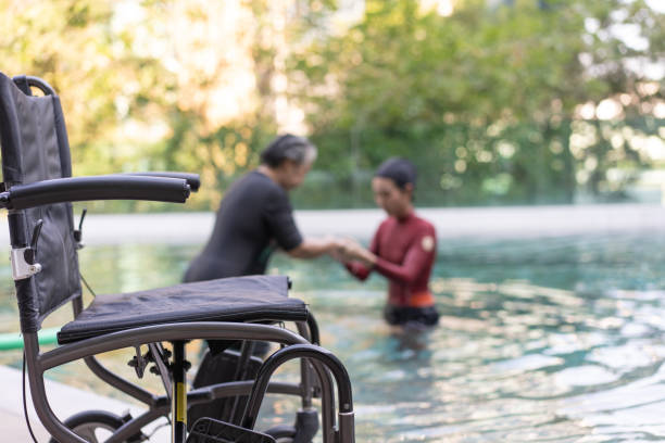 выборочный фокус на инвалидной коляске физиотерапевта, помогающего пожилой женщине в аква, пожилым женщинам и зрелым женщинам, занимающим� - physical therapy hydrotherapy swimming healthcare and medicine стоковые фото и изображения