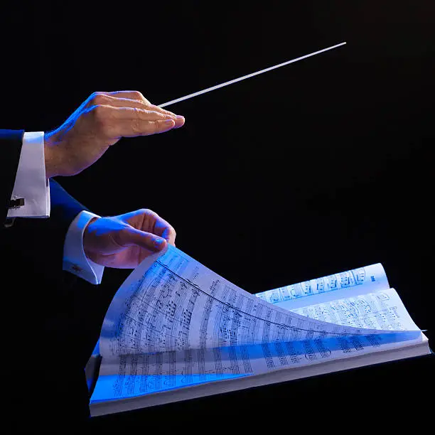 Photo of Hands of a conductor with a baton and musical book