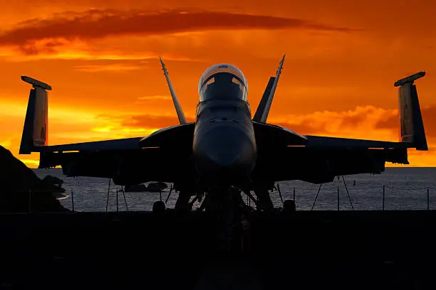 A modern jet fighter parked on the deck of an aircraft carrier with dramatic sky.