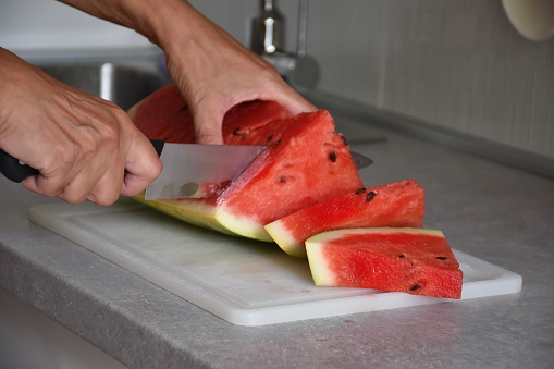 Woman's hands cutting watermelon on plastic cutting board in the kitchen