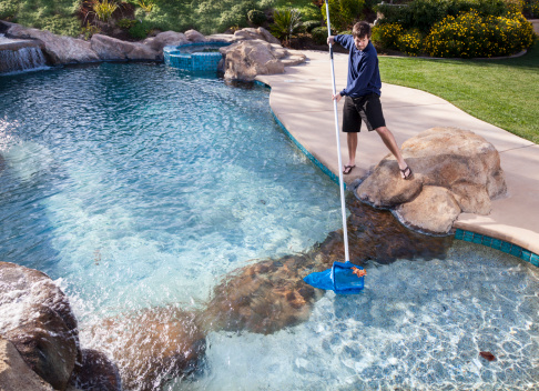 Man cleaning swimming pool with net. Removing leaves