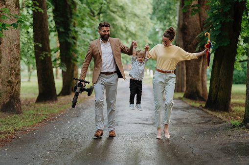 Rear view of young family with little son on a walk in a city park after work. Working parents spending time with their son after work day. Parents pick up kid from daycare.