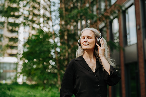 Mature middle-aged caucasian woman listening to the music radio song podcast e-book on smartphone in headphones, choosing sound track in mobile application isolated in white background