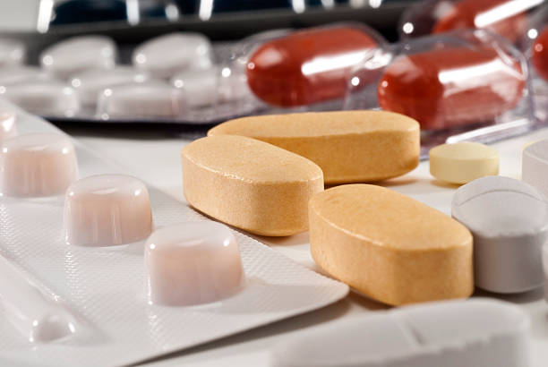 Close-up of green and white capsule pills in partially opened blister packs, with one loose capsule on a white background.