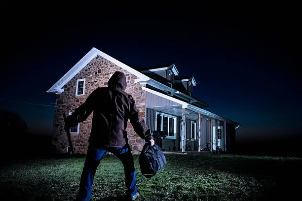 A photograph of a burglar outside a house at night.