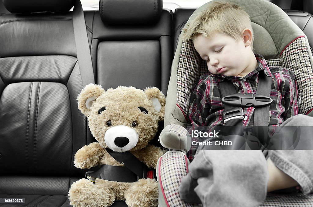 Cozy and safe Child sound a sleep seating in the car seat next to buckled up teddy bear, safety first. Shallow DOF, natural light. Car Safety Seat Stock Photo