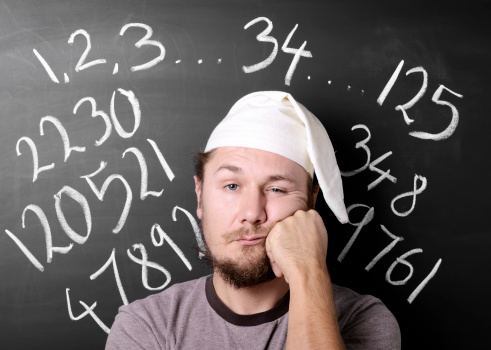 Very tired man counting endlessly trying to fall a sleep, against chalkboard.