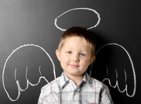 Little boy with angel wings and aureola drawing on the chalkboard.