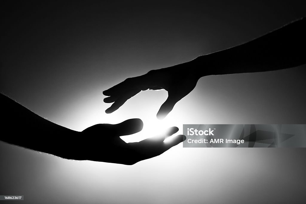 Black and white image of two hands reaching out Male and female hands reaching out for each other. Black and white image with light behind them. Conceptual image that pertains to support, love, marriage and togetherness.    Support Stock Photo