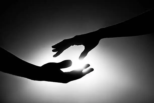 Male and female hands reaching out for each other. Black and white image with light behind them. Conceptual image that pertains to support, love, marriage and togetherness.   