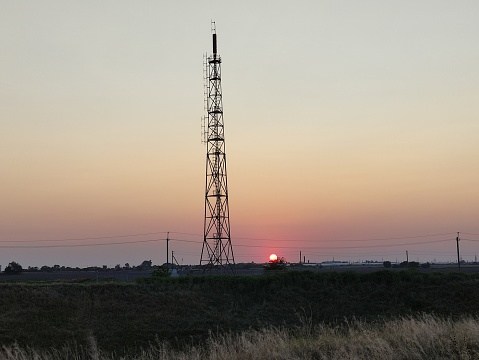 Evening field and road, against the background of the telecommunication tower at sunset