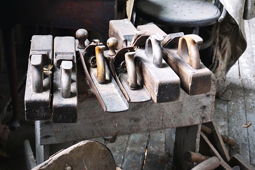 A collection of vintage carpenter's block planes lined up on a simple wooden bench in a dusty workshop