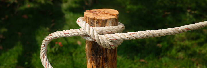 Close up white rope twisted on wooden pole with green bokeh background